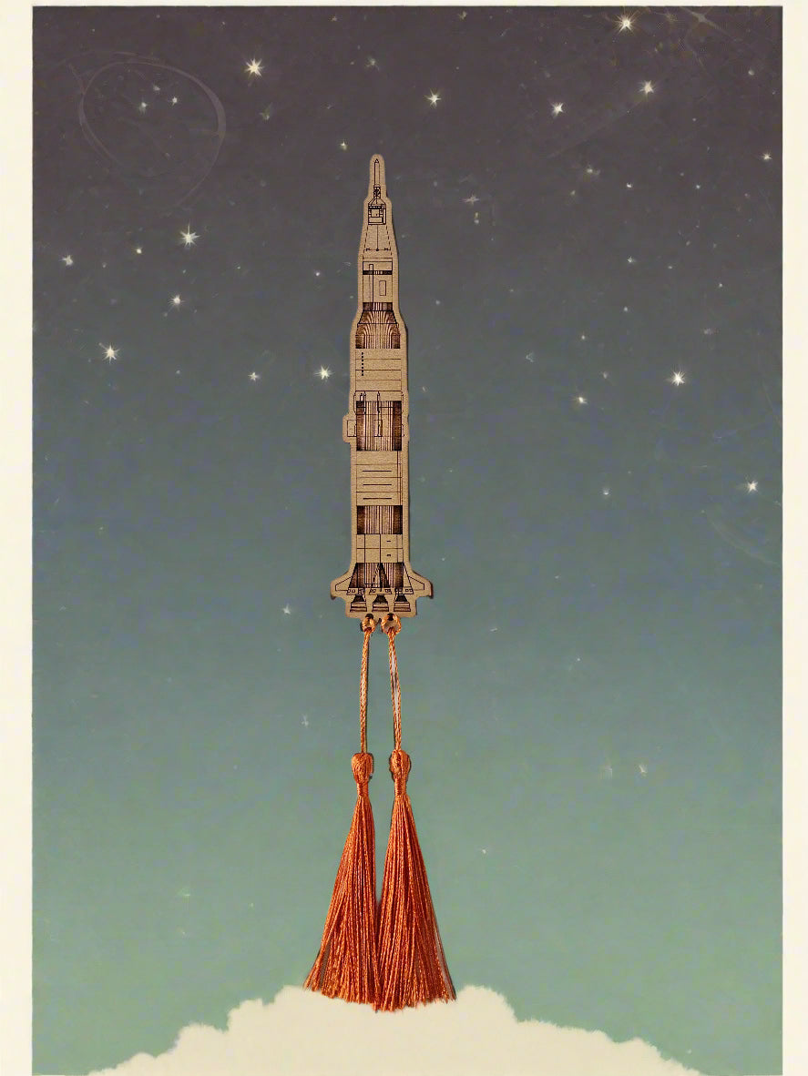 A bookmark that is laser-engraved to look like the Saturn V rocket with dual orange tassels that look like it is blasting off into space