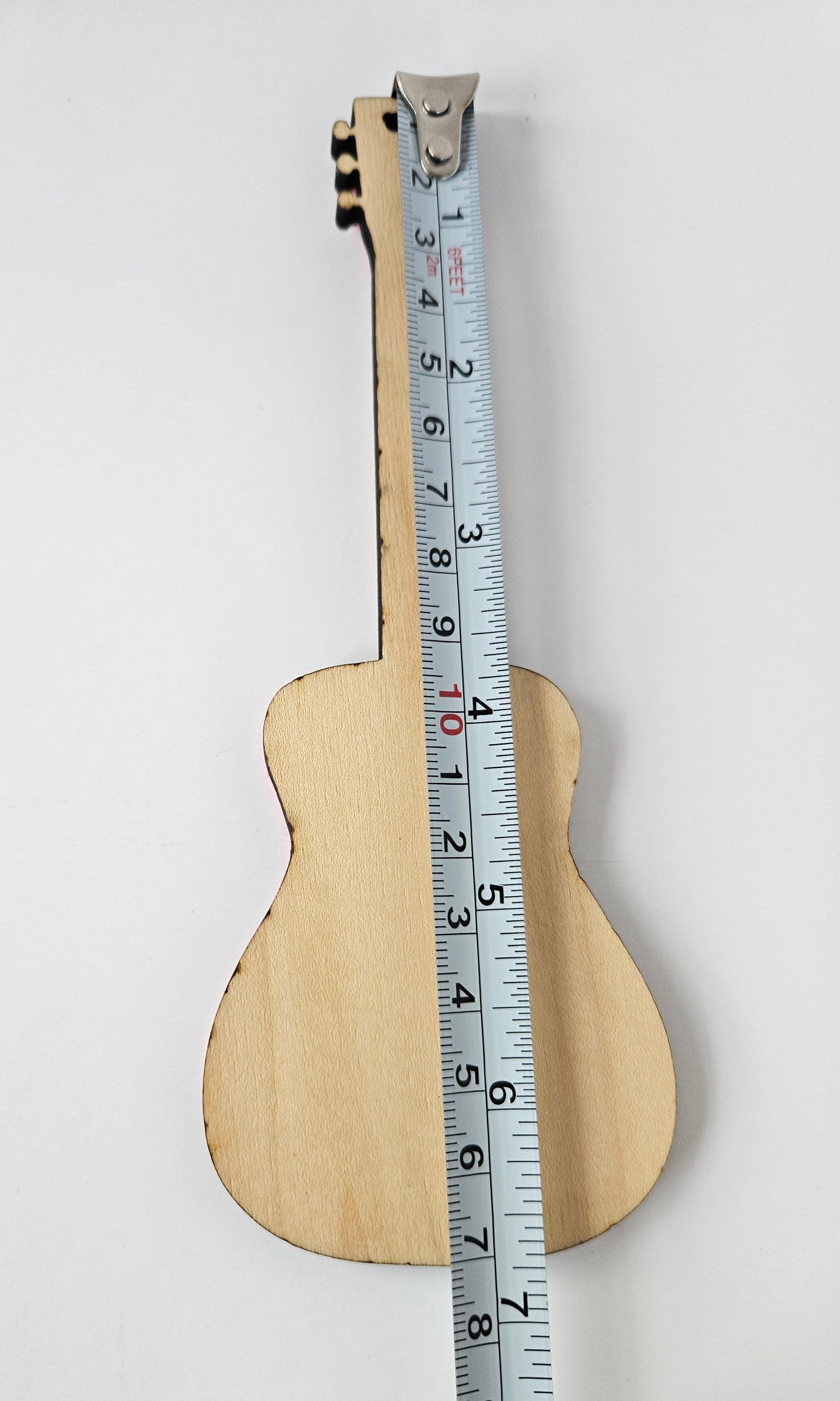 Small wooden guitar, back view, with a tape measure for scale on a white background