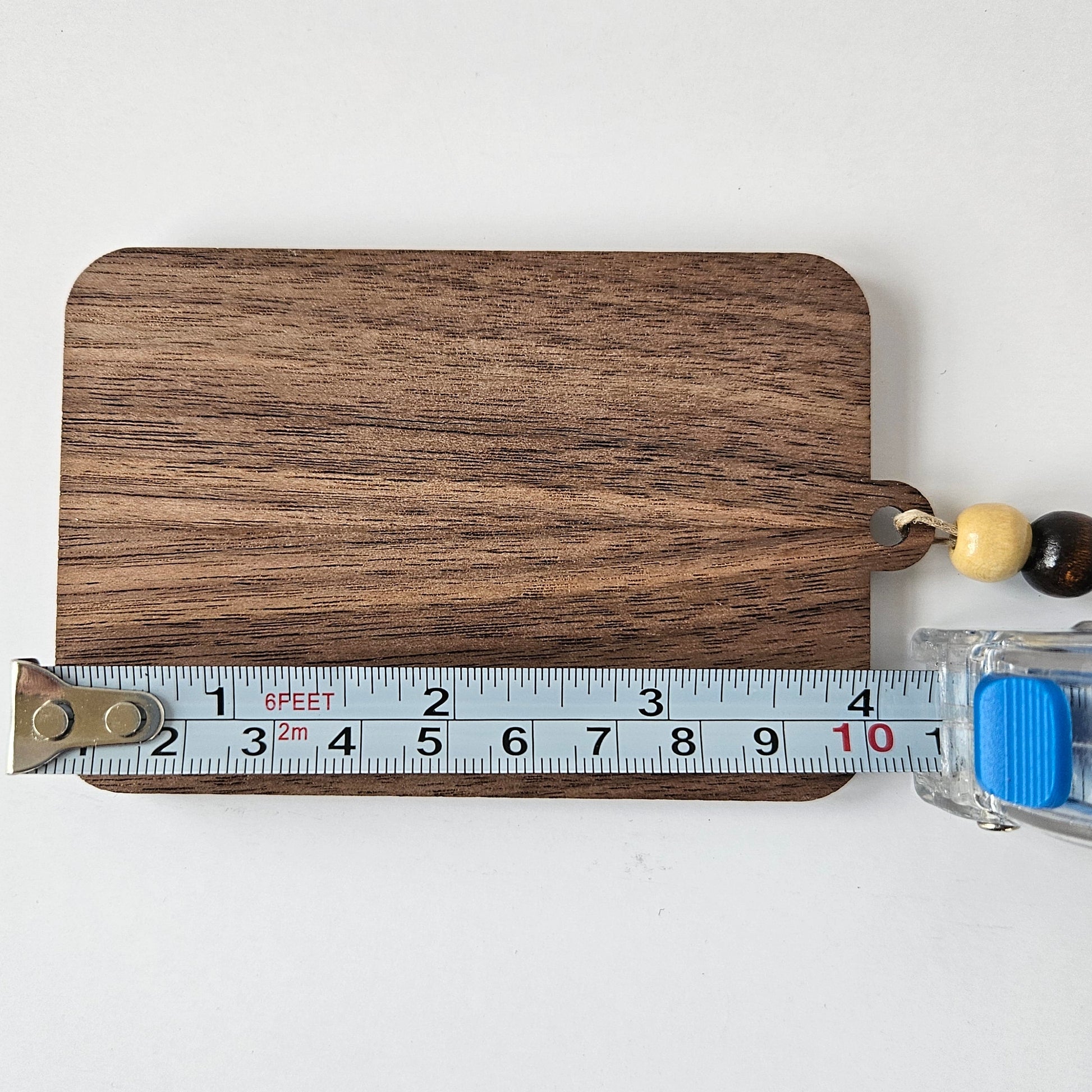 Wooden hanging gift card holder with beads and a tape measure for scale on a white background