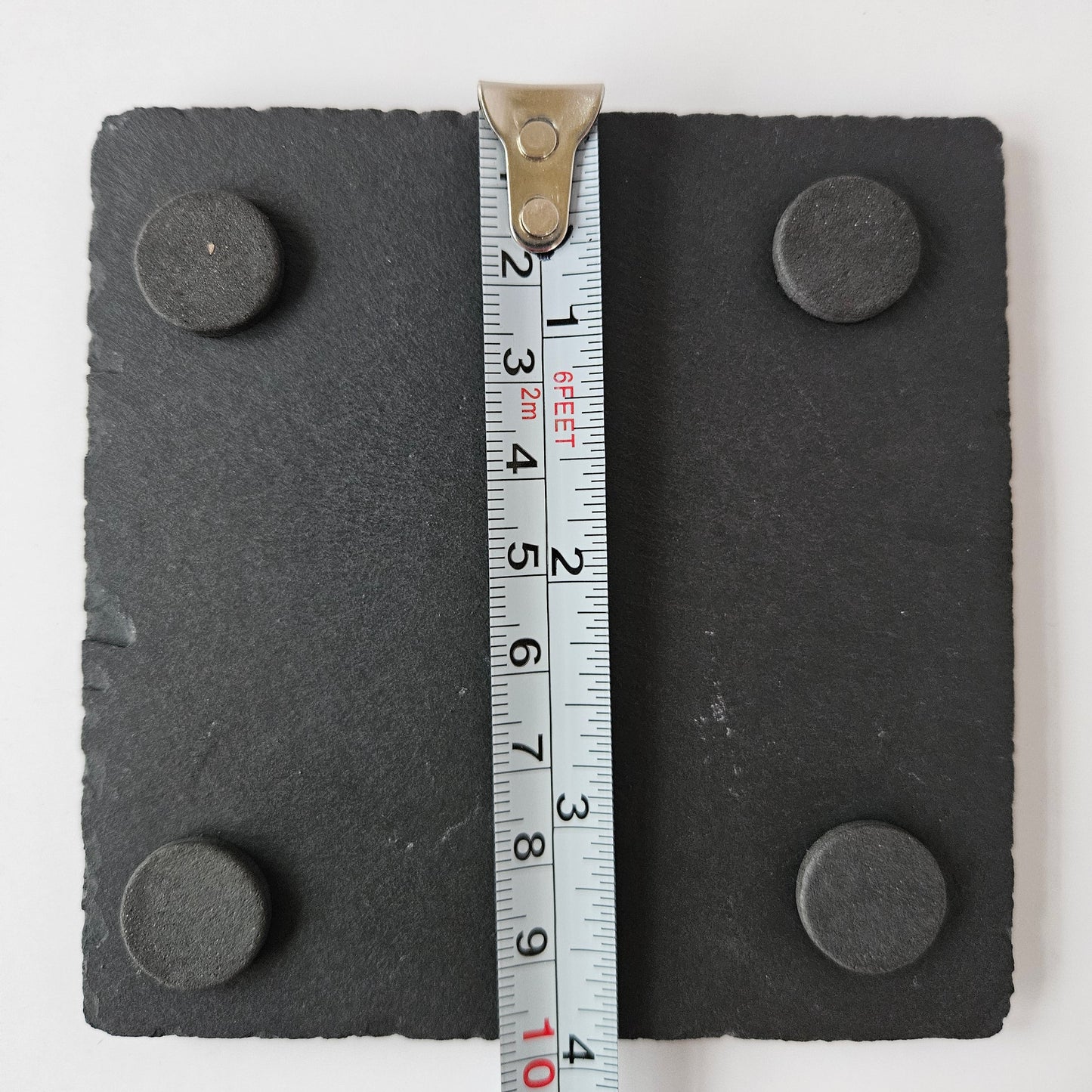 Back of slate coaster showing four pads, measured by a ruler on a white background